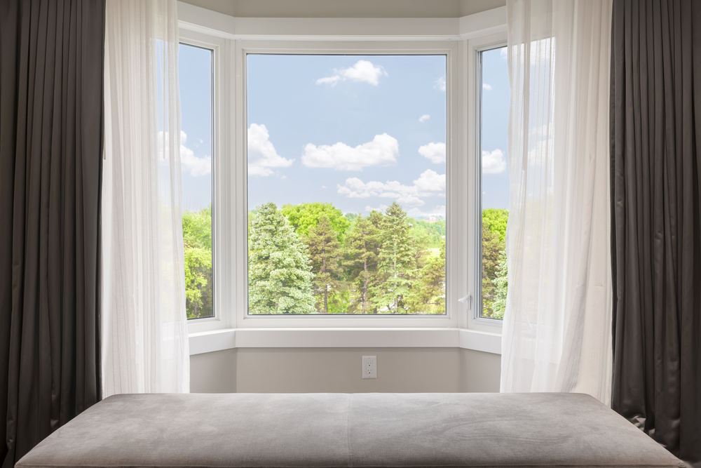 Bay window with drapes, curtains and view of trees under summer sky (Bay windows vs bow windows)