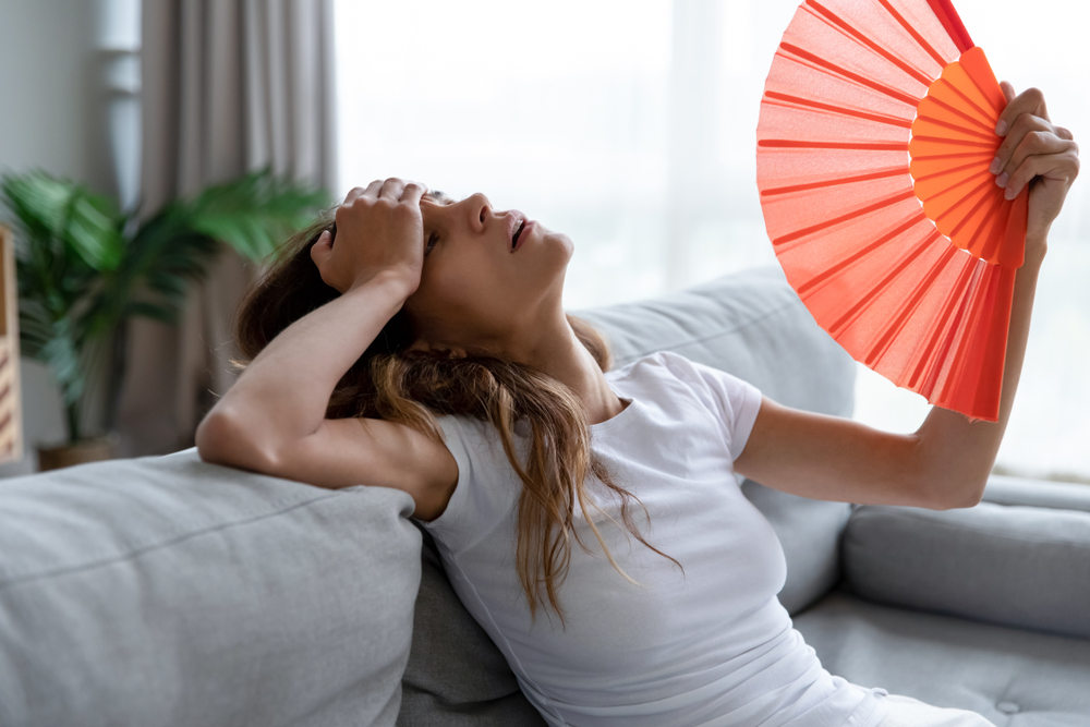 Lady hot in summer heat inside home (How Replacement Windows Can Keep Your Home Cool in the Summer)