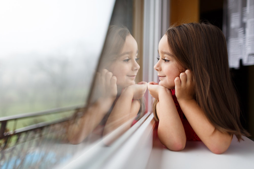 Girl looking through window (Are Energy Efficient Windows Worth the Investment)
